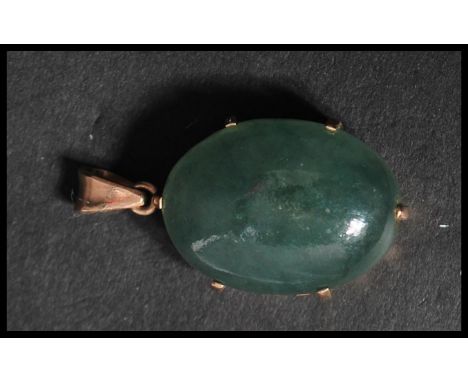 A vintage unmarked but tests as 9ct gold jade pendant. The large jade cabochon set to a pierced gold mount with bail loop ato