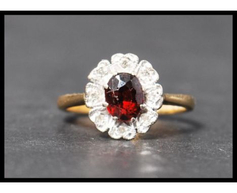 A hallmarked 18ct gold diamond and garnet stone cluster ring having a central faceted stone with a halo of illusion set diamo