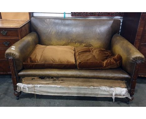 Early 20th century oak framed brown leather two-seat sofa on turned supports to castors