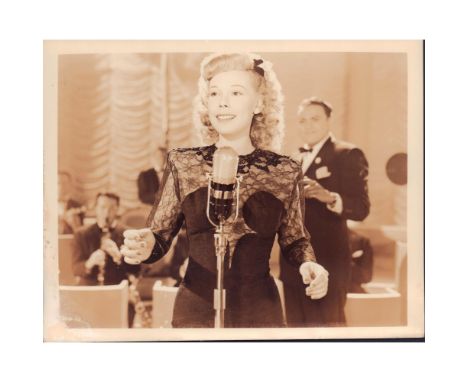 Featuring pretty lady at microphone and slightly out of focus gentleman behind her wearing a smile. Presumably a film still o