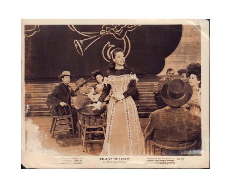 Photo of a scene from the film 'Belle of the Yukon', featuring a beautiful actress singing. Title of the film and other infor