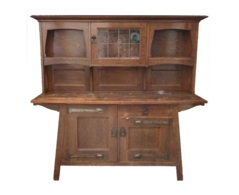 A LIBERTYS OF LONDON OAK ARTS AND CRAFTS SIDEBOARD the overhanging cornice above a leaded glass door, flanked by open shelves