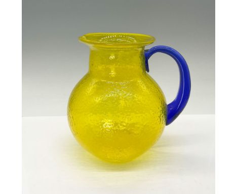 This vibrant lemon peel-textured glass pitcher features a striking, hand-crafted cobalt blue handle and a sleek, modern silho