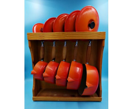 Le Creuset - Graduated set of five lidded saucepans in burnt orange on a pine display stand (largest pan has enamel loss at t
