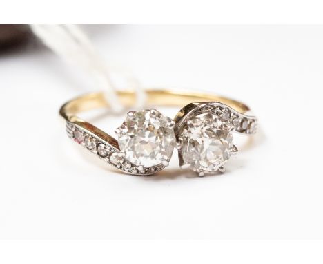 A diamond two-stone cross over ring, diamond set shoulders, the two round old cut diamonds weighing approx 1.50 carat, 0.75 c