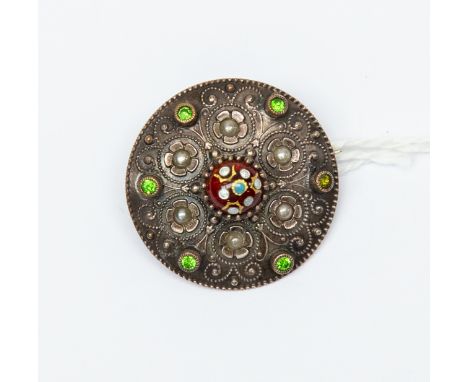 A white metal target brooch, circa 1900, ropework floral and scroll design with green facet cut insets and a red cabouchon an