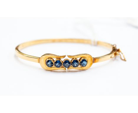 A yellow gold and sapphire hinged bangle, set with five round cut sapphires, tests as approx 14k, approx 10 grams