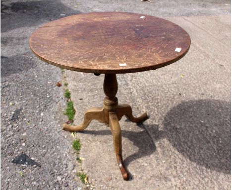 A George III oak tilt-top tripod table, circa 1820, the circular plank top raised on a baluster turned column, standing on th