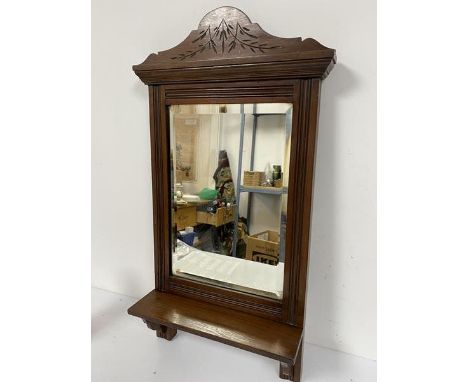 An Edwardian walnut shaving mirror with arched carved surmount and bevelled glass plate, with open shelf, on shaped supports 
