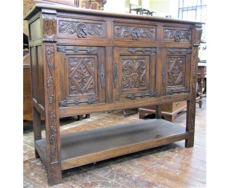 An Old English side cupboard, the front elevation enclosed by three carved and panelled doors and three further drawers, with