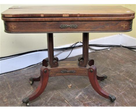 A Regency rosewood foldover top card table raised on four scrolled supports and platform base, with sabre legs and applied de