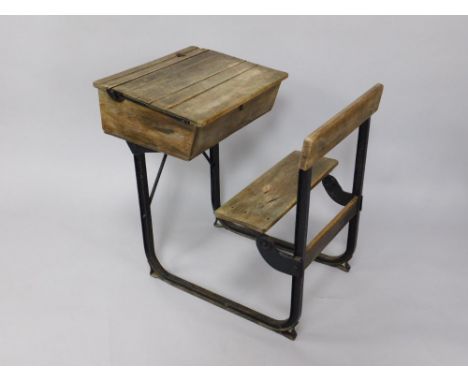 An early 20thC oak and iron framed child's school desk, with a writing slope, pen and inkwell recess, and folding chair.