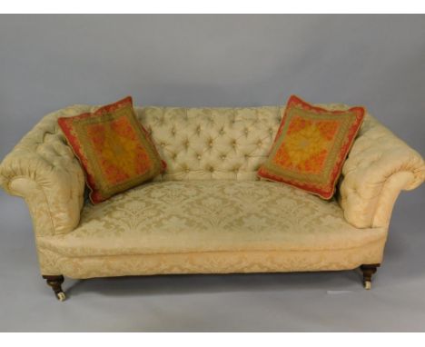 A Victorian oak framed Chesterfield sofa, upholstered in button back floral gold upholstery, raised on turned legs, on castor