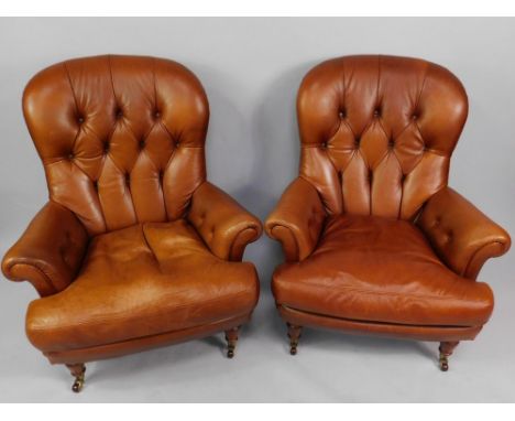 A pair of button back tan leather armchairs, raised on turned legs, brass capped on castors.