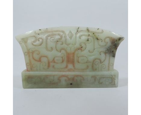 A Chinese jade coloured stone axe head, with russet and black inclusions, carved throughout with geometric stylised scrolling