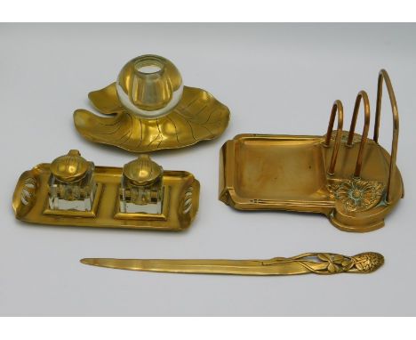 Four art nouveau brass desk items including a match stand, a WMF style letter rack, a pair of ink wells & a letter opener mar