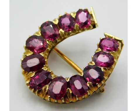 A yellow metal horse shoe shaped brooch set with ruby, tests electronically as 14ct gold, one ruby has crack, 21mm x 19mm, 4.