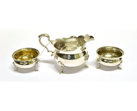 A SILVER SMALL COMPRESSED-ROUND CREAM JUG AND A PAIR OF CAULDRON-SHAPED SALTS The cream jug with a leaf-capped double-scroll 