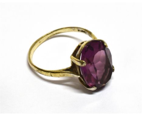 AN OVAL AMETHYST-COLOURED PASTE SINGLE STONE RING the mixed-cut stone claw set in white between tapering shoulders on a 'D' s