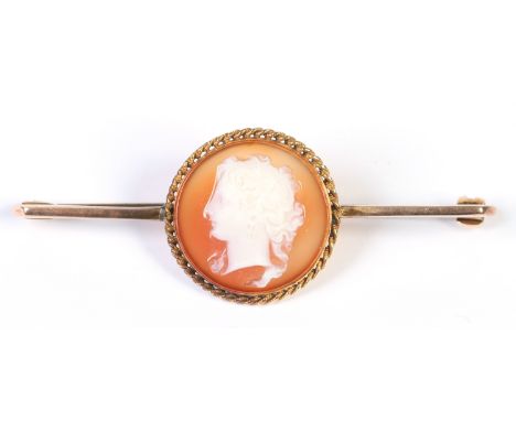A Victorian yellow metal bar brooch set with a circular carved hardstone cameo depicting the profile portrait of a Classical 