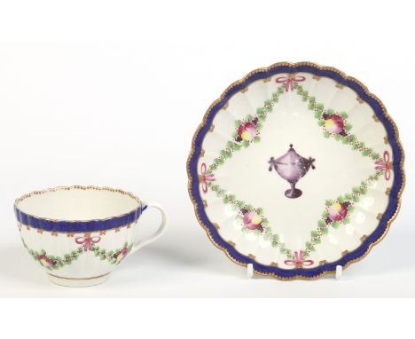 A Worcester fluted teacup and saucer. With gilt dentil rims, wet blue borders, enamelled with fruit swags supported on ribbon
