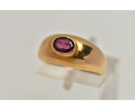 A YELLOW METAL GARNET SET RING, set with an oval cut garnet in a raised collet setting, to a tapering polished band, unmarked