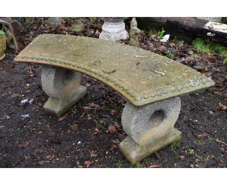 A WEATHERED COMPOSITE CURVED GARDEN BENCH, on circular shaped supports, length 122cm x depth 42cm x height 47cm