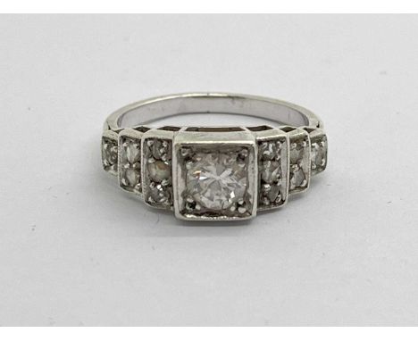 An Art Deco Diamond Set Ring, of stepped design, the brilliant cut stone between diamond chip inset shoulders (finger size M)