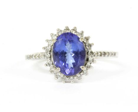An 18ct white gold tanzanite and diamond halo cluster ring, an oval mixed cut tanzanite, 9.02 x 6.84 x 4.28mm, claw set to a 