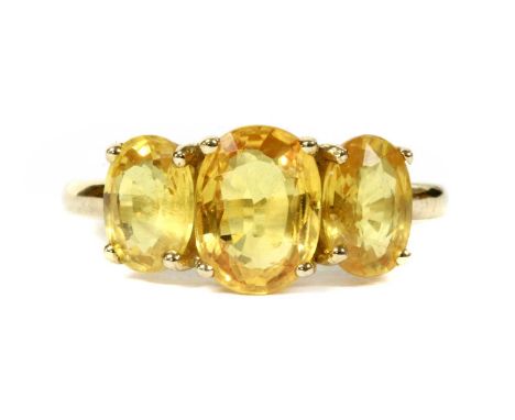 A gold three stone yellow sapphire ring, a graduated row of oval mixed cut yellow sapphires, all claw set to a plain 'D' sect