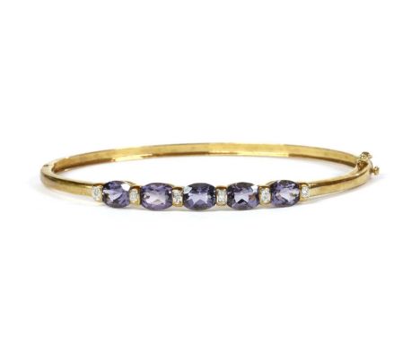A 9ct gold iolite and diamond bangle, the oval hinged bangle with a row of oval mixed cut iolites claw set to the top half, w
