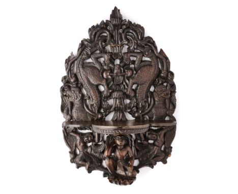 AN ANGLO-BURMESE CARVED WOOD WALL BRACKET, CIRCA 1900 the lobed shelf supported by a crouching figure flanked by a pair of my