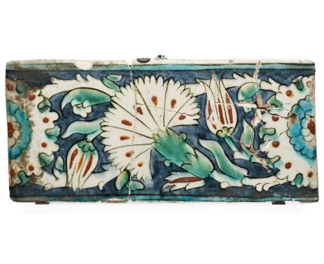 AN IZNIK BORDER TILE, OTTOMAN ANATOLIA, 17TH CENTURY underglaze painted fritware, decorated with a scrolling carnation, tulip