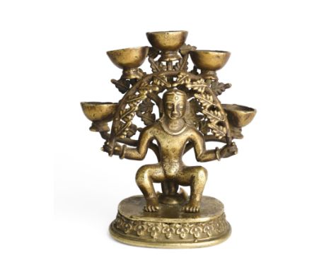 A BRONZE TEMPLE LAMP, NEPAL, LATE 19TH CENTURY in the form of a figure under a leafy arch, holding five burner holders, 13.5c