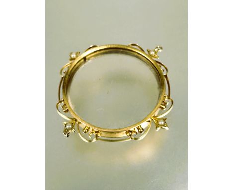 A Edwardian yellow metal circular portrait pendant with scrolling border set four star set seed pearls with original glass pa