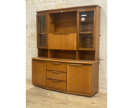 A mid century teak two part high board, the illuminated top section fitted with two glazed doors, fall front cocktail cabinet