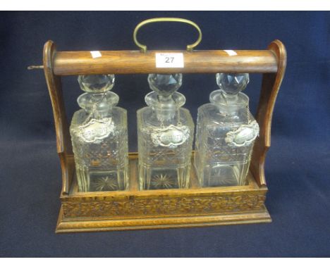 Early 20th Century oak three bottle tantalus with three cut glass spirit decanters having silver plated decanter labels. (B.P