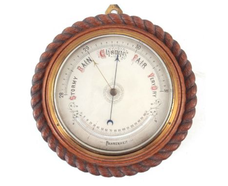 AN EARLY 20th CENTURY OAK CASED ROPE EDGE ANEROID BAROMETER having a silvered engraved calibrated dial and curved thermometer