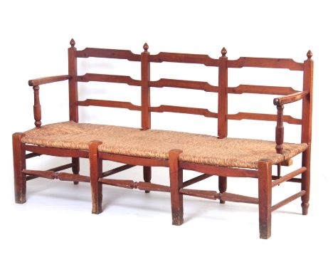 A PITCH PINE ARTS AND CRAFTS STYLE  RUSH SEATED BENCH with shaped ladder back and open arms standing on square tapering legs 