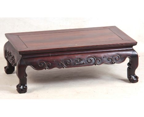 A 19TH CENTURY CHINESE HARDWOOD LOW OCCASIONAL TABLE with panelled top and shaped scroll carved base on short legs with claw 