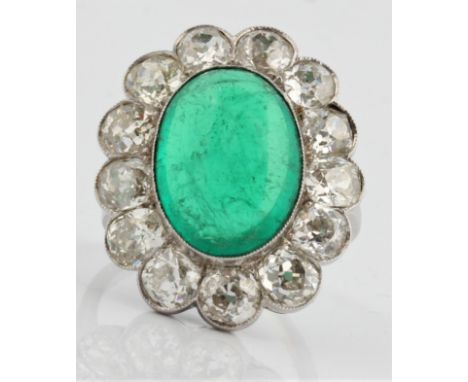 An emerald and diamond cluster ring, set with a central oval emerald cabochon, measuring approx. 16x12x6mm, surrounded by a b