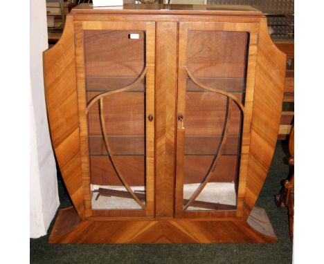 An Art Deco walnut two-door glazed display cabinet, the body of shield form with two shelves