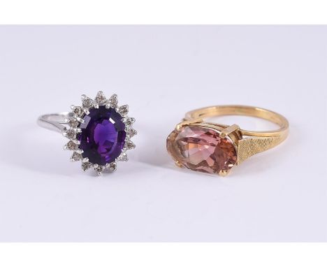 
	
		AN AMETHYST AND DIAMOND CLUSTER RING AND A PINK TOURMALINE DRESS RING 
		The first with a mixed oval cut amethyst within