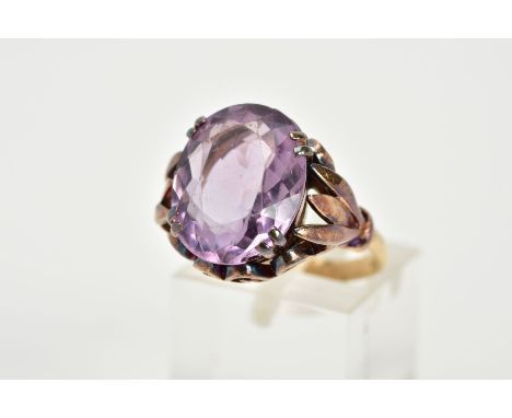 A 9CT GOLD AMETHYST RING, designed with a double claw set, oval cut amethyst, within an openwork scroll gallery and trifurcat