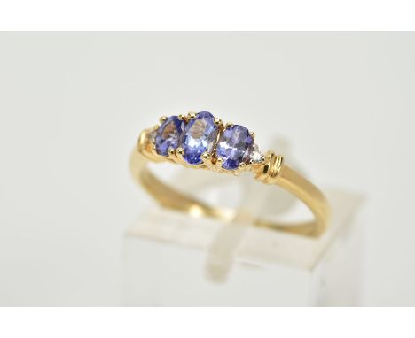 A 14CT GOLD THREE STONE TANZANITE RING, designed with three graduated, oval cut tanzanite stones, flanked with single cut dia