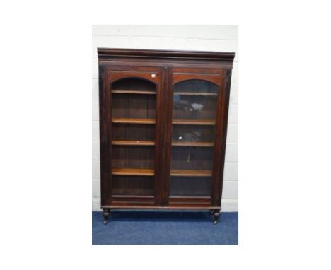 AN EDWARDIAN MAHOGANY DOUBLE DOOR BOOKCASE on turned legs with ceramic casters, width 130cm x depth 33cm x height 182cm (alte