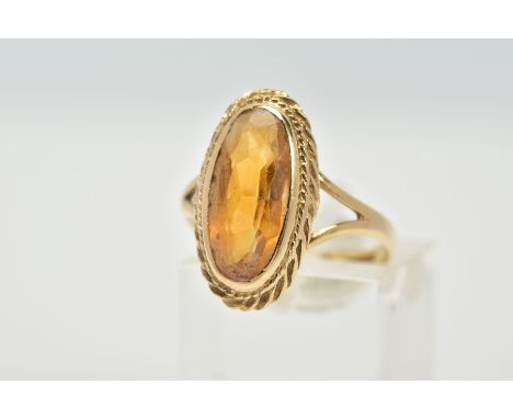 A 9CT GOLD CITRINE RING, designed with an oval cut citrine, within a collet mount and rope twist surround, bifurcated shoulde