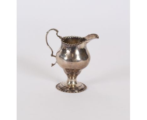 A George III silver helmet shaped cream jug, having serrated borders and harp shape handle, London 1775, 10cm high