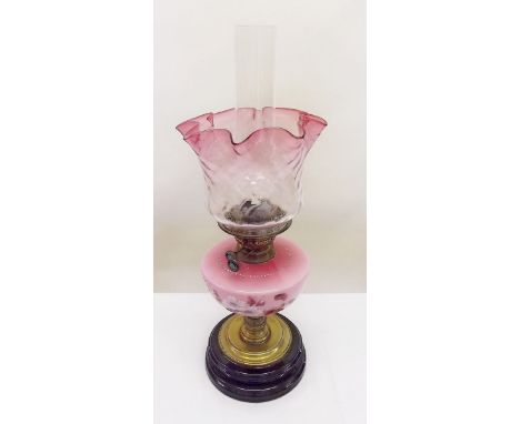 A Victorian oil lamp with floral painted pink reservoir and cranberry tinted shade