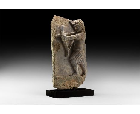 1st-4th century AD. A carved schist frieze fragment depicting a kilted figure with bare torso and shoulder-length hair advanc